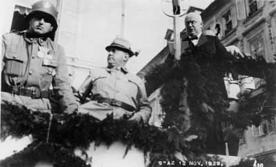 Die Heimwehrführer Ernst Rüdiger Starhemberg und Walter Pfrimer mit dem steirischen Landeshauptmann Anton Rintelen. Graz, 12. November 1929. Blick von unten auf die Tribühne, wo die drei Männer stehen. Starhemberg mit Uniform und Helm, Pfrimer mit Trachtenhut und Rintelen im schwarzen Anzug.