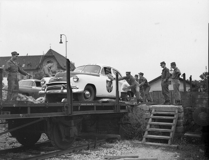 Am Frachtenbahnhofsgelände Gersthof (Wien) verladen US-Soldaten Militärpatrouillenautos auf offene Güterwaggons. August 1955. Ein weißer Militärpolizei-PKW auf einem Wagon und einige Soldaten sind zu sehen.