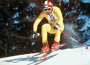 Franz Klammer in hellgelben Ganzkörperanzug mit rot-weiß-rotem Helm springt mit der Startnummer 15 ins Bild.