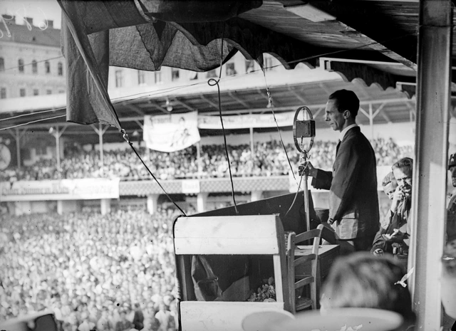 Der aus Deutschland angereiste Reichspropagandaleiter der NSDAP, Joseph Goebbels, spricht etwa zwei Stunden vor 16–20.000 Zuhörern in der Engelmann-Arena, einem Sport- und Eislaufplatz in Wien, Hernals. Sonntag Nachmittag, 18. September 1932. Goebbels rechts am Rednerpult vor einem großen Mikrofon. Blick in das offene Stadion das ganz gefüllt ist. 