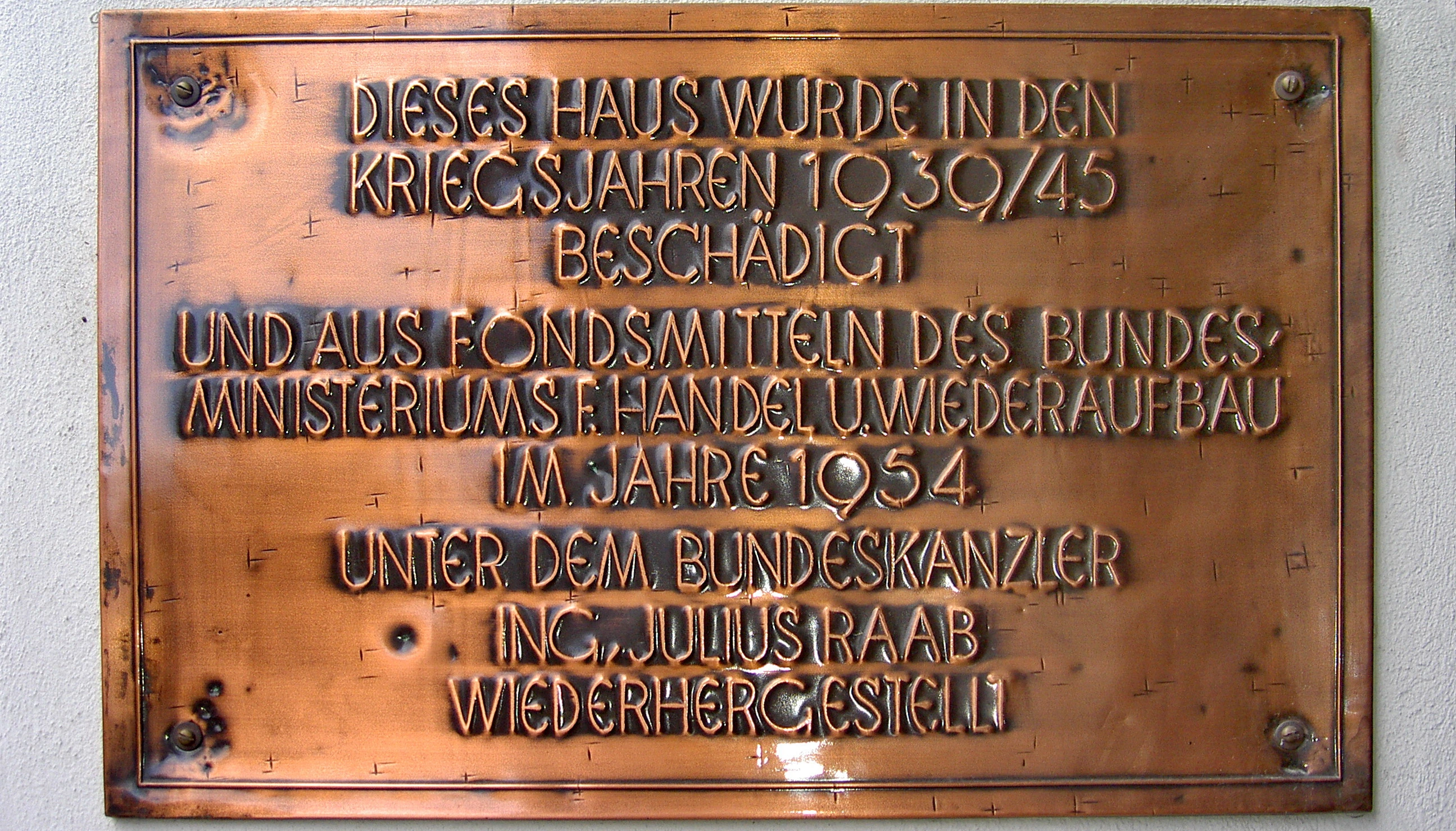 Renovierung kriegsbeschädigter Wohnbauten. Kupferne Tafel an einer Haus: "Dieses Haus wurde in den Kriegsjahren 1939/45 beschädigt und aus Fondsmitteln des Bundesministerium f. Handel u. Wiederaufbau im Jahre 1954 unter dem Bundeskanzler Ing. Julius Raab wiederhergestellt."