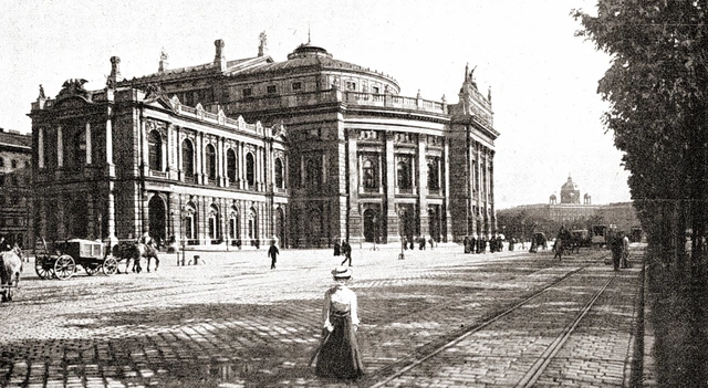 Foto von der Ringstraße gesehen. Ein Pferdefuhrwerk aber auch Passanten sind auf der breiten Straßen vor dem Theater zu sehen.