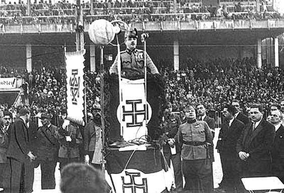 Engelbert Dollfuß bei seiner programmatischen "Trabrennplatzrede" am 11. September 1933 in Wien. Dollfuß am mit Krukenkreuz geschmückten Rednerpult vor gefüllter Trabrennplatztribüne.