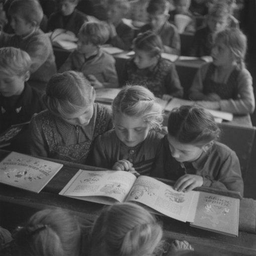 Mädchen lesen Bücher an Schultischen sitzend