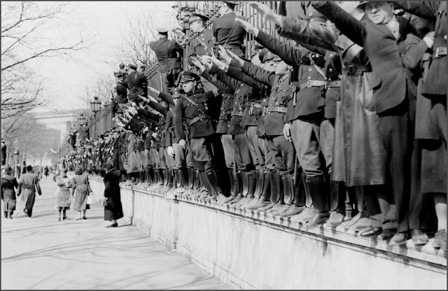 Auf der Umfriedung des Heldenplatzes drängen sich viele Menschen, darunter auch zahlreiche Polizisten, die den rechten Arm zum Hitlergruß erhoben haben.