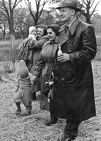 Frauen mit Kindern und ein Mann mit einem Babyflascherl gehen über ein Feld.