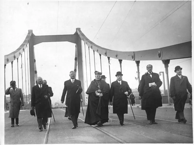 Eröffnung der Wiener Reichsbrücke. In der Mitte Bundeskanzler Kurt Schuschnigg, Kardinal Theodor Innitzer und Bundespräsident Wilhelm Miklas mit Melone. Wien, am 10. Oktober 1937. Die Herrschaften gehen nebeneinander über die Brücke.