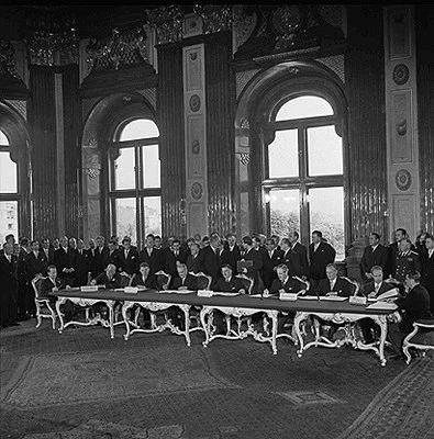 Außenminister Leopold Figl unterzeichnet für Österreich als Letzter den Staatsvertrag mit grüner Tinte. Schloss Belvedere, Wien, am Sonntag, den 15. Mai 1955. Blick in den Saal des Schloss Belevdere mit den Politikern an den Tischen. Hinter den sitzenden auch stehende Politiker.