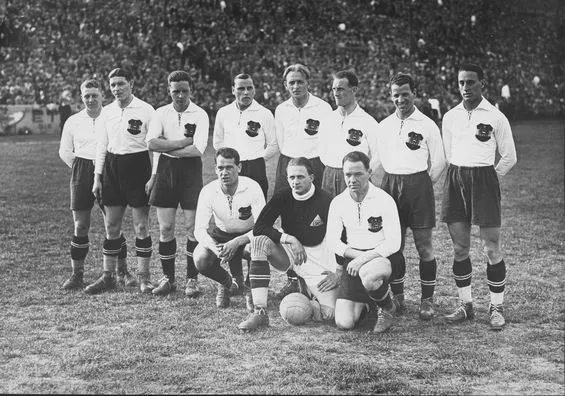 Das "Wunderteam" beim Spiel gegen Ungarn am 24. April 1932 in Wien. Stehend von links: Schramseis, Nausch, Hofmann, Zischek, Sindelar, Braun, Schall, Vogel; kniend von links: Gschweidl, Hiden, Blum. Gruppenfoto am Spielfeld vor voller Tribüne. Spieler in schwarzen Hosen und weißen Dressen.