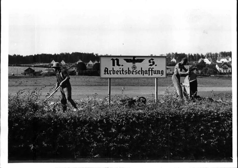 Aufnahme vom Baubeginn der Wienfluss-Regulierung bei Pressbaum (Niederösterreich). 27. Juli 1938. Zwei Arbeiter bei einem Schild: "n.s. Arbeitsbeschaffung"