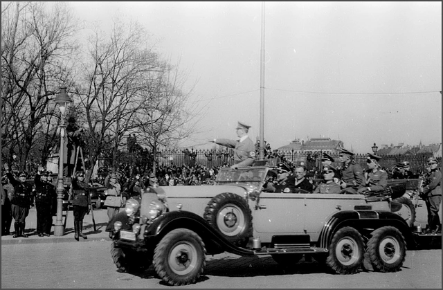 Auf der Schwarz-Weiß-Fotografie sieht man Adolf Hitler mit erhobenem rechtem Arm, wie er in seinem Auto an der Menschenmenge vorbeifährt.