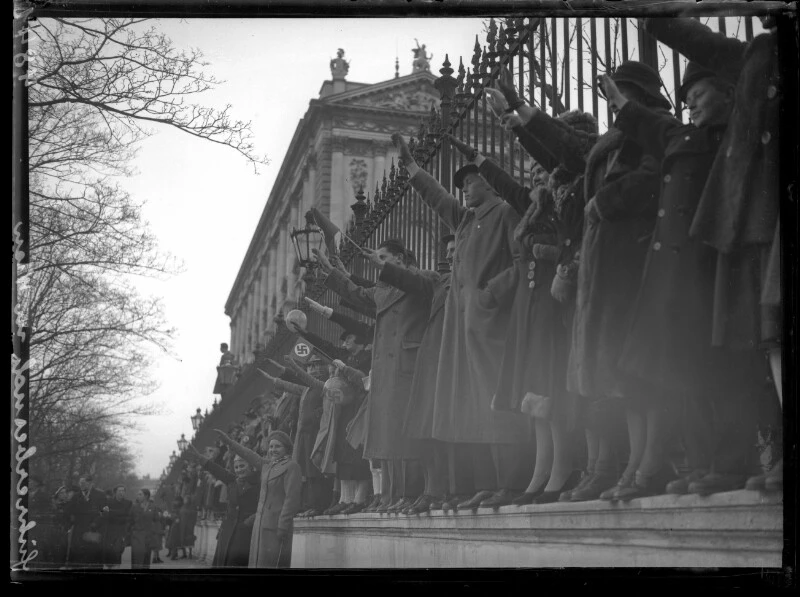 Begeisterung beim Einzug Adolf Hitlers in Wien, an der Ringstraße. Im Hintergrund die Hofburg. 15. März 1938. Frauen in Mänteln beim Zaun der Neuen Burg an der Ringstraße mit erhobenen Armen zum Hitlergruß