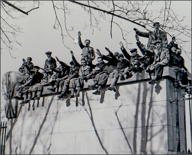 Schwarz-Weiß-Foto. Wien, 15. März 1938. Zahlreiche Menschen sitzen und stehen auf der Umfriedung des Wiener Heldenplatzes und haben den rechten Arm zum Hitlergruß erhoben.