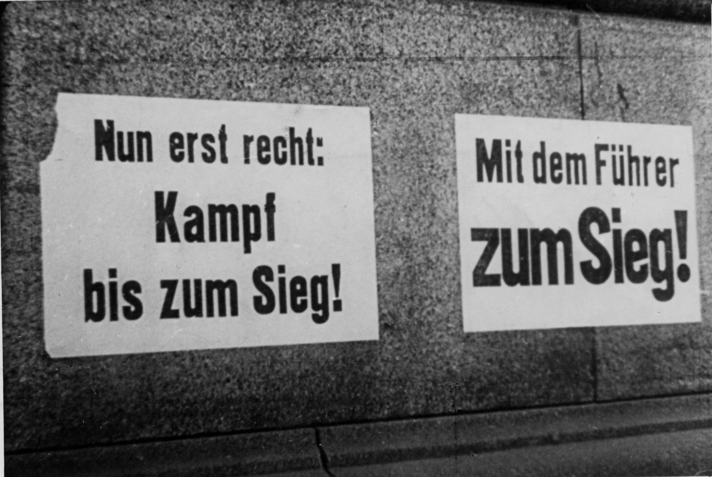 Propagandaplakate an Häuserwänden: "Nun erst recht: Kampf bis zum Sieg!" "Mit dem Führer zum Sieg!" 