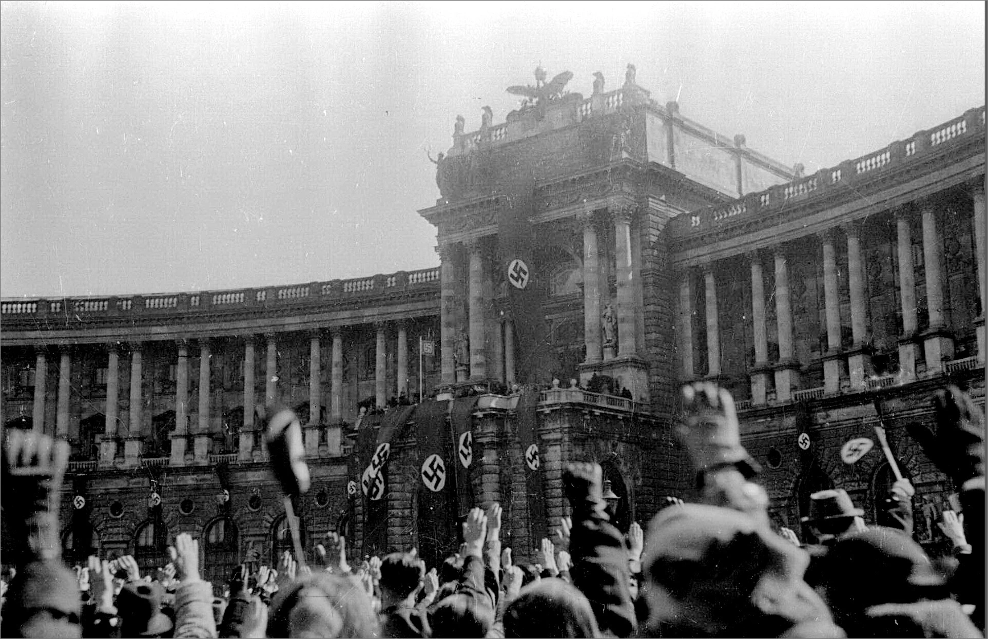 Schwarz-Weiß-Foto vom Wiener Heldenplatz mit Blick auf die Neue Hofburg, die mit Hakenkreuzfahnen geschmückt ist.