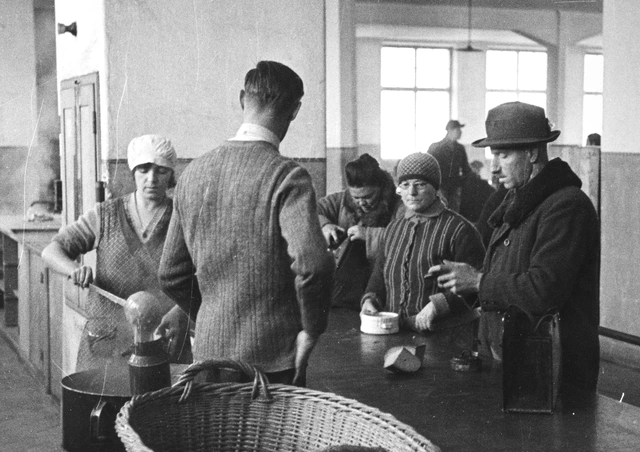 Anstellen um eine warme Mahlzeit. Steyr, 1932. Frauen und Männer erhalten bei der Ausgabe in einer Großküche Suppe und Brot in ihre mitgebrachten Kannen und Töpfe.